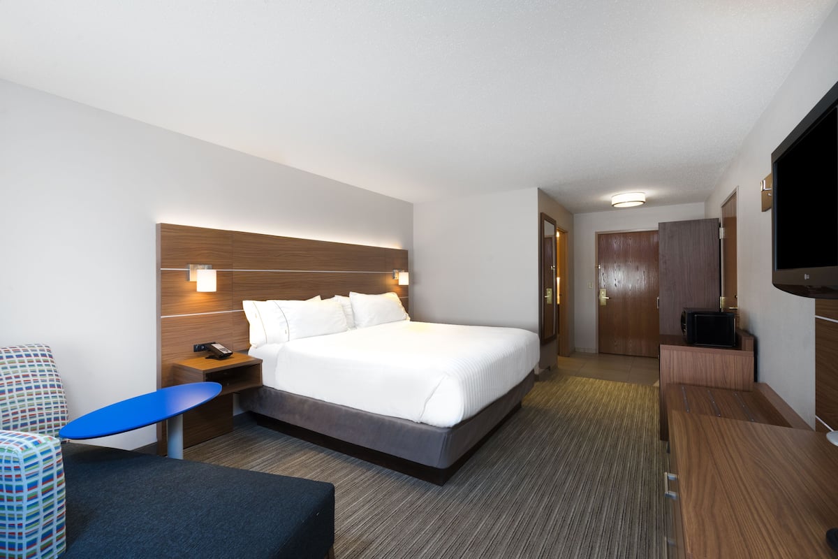 A hotel room with a large bed, a desk, a chair, a TV, and a wardrobe.
