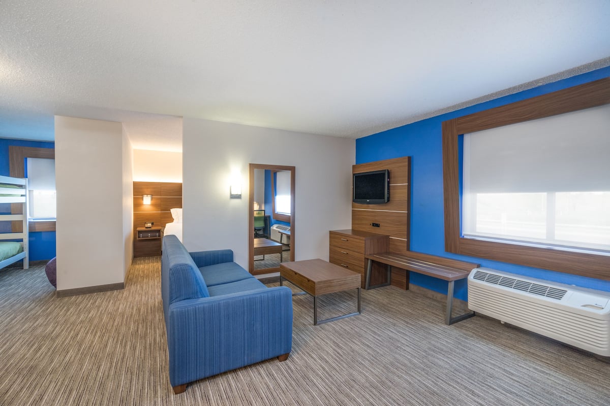 A modern hotel room with a blue sofa, a wooden desk, a TV, and a large window.