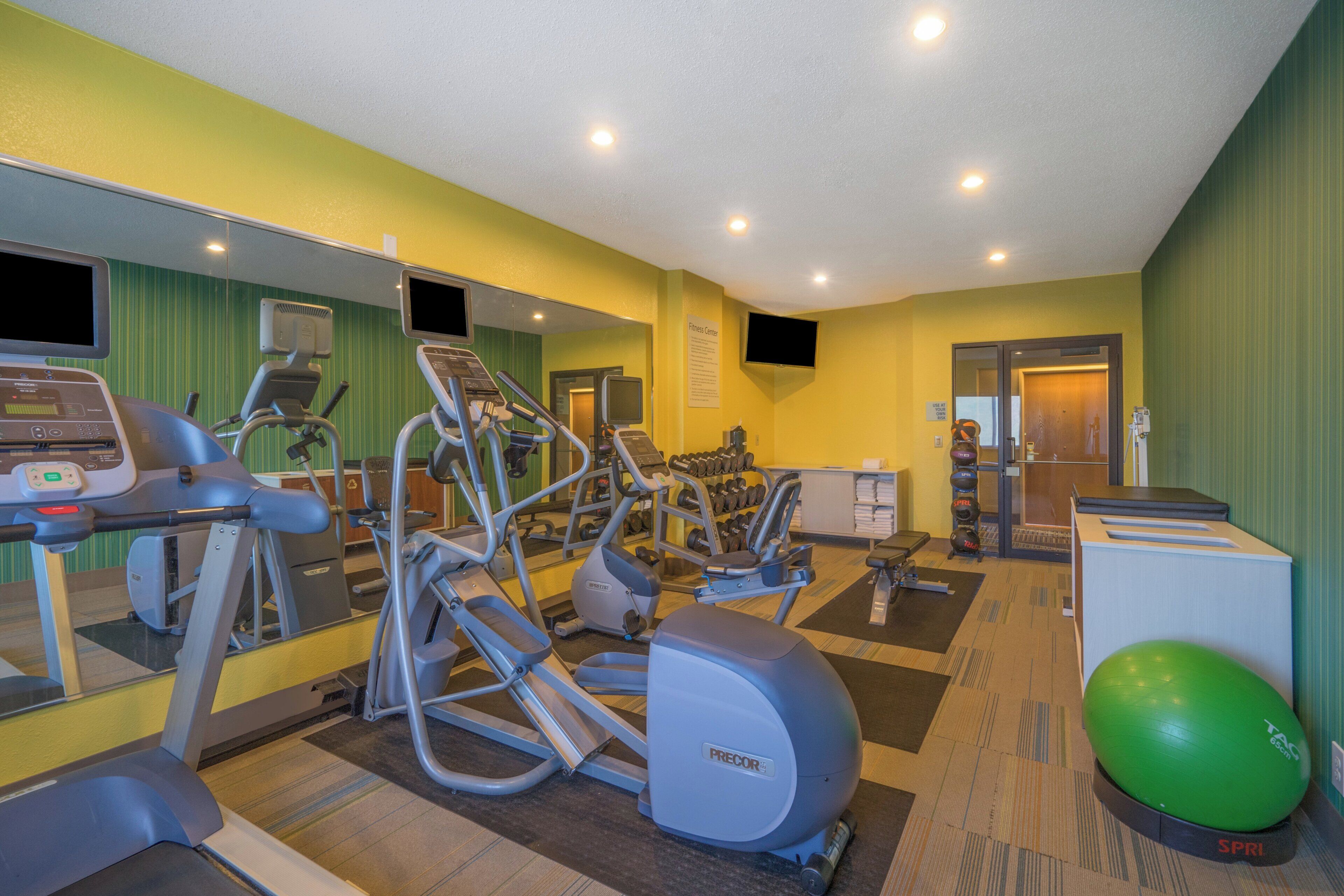 A fitness center with cardio machines, free weights, and a mirrored wall.