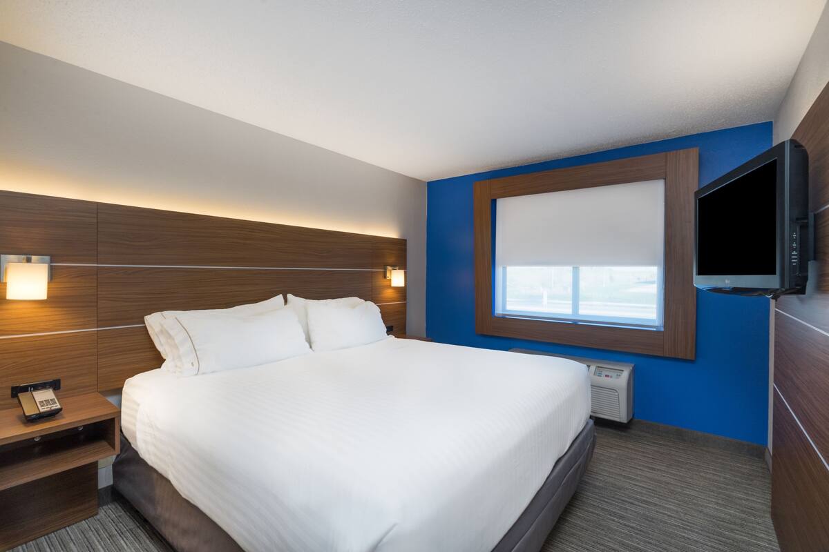 A modern hotel room with a large bed, bedside lamps, a flat-screen TV, and a window with blinds.