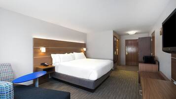 Une chambre d’hôtel comprenant un lit, une table de chevet, une télévision et un bureau avec une chaise.