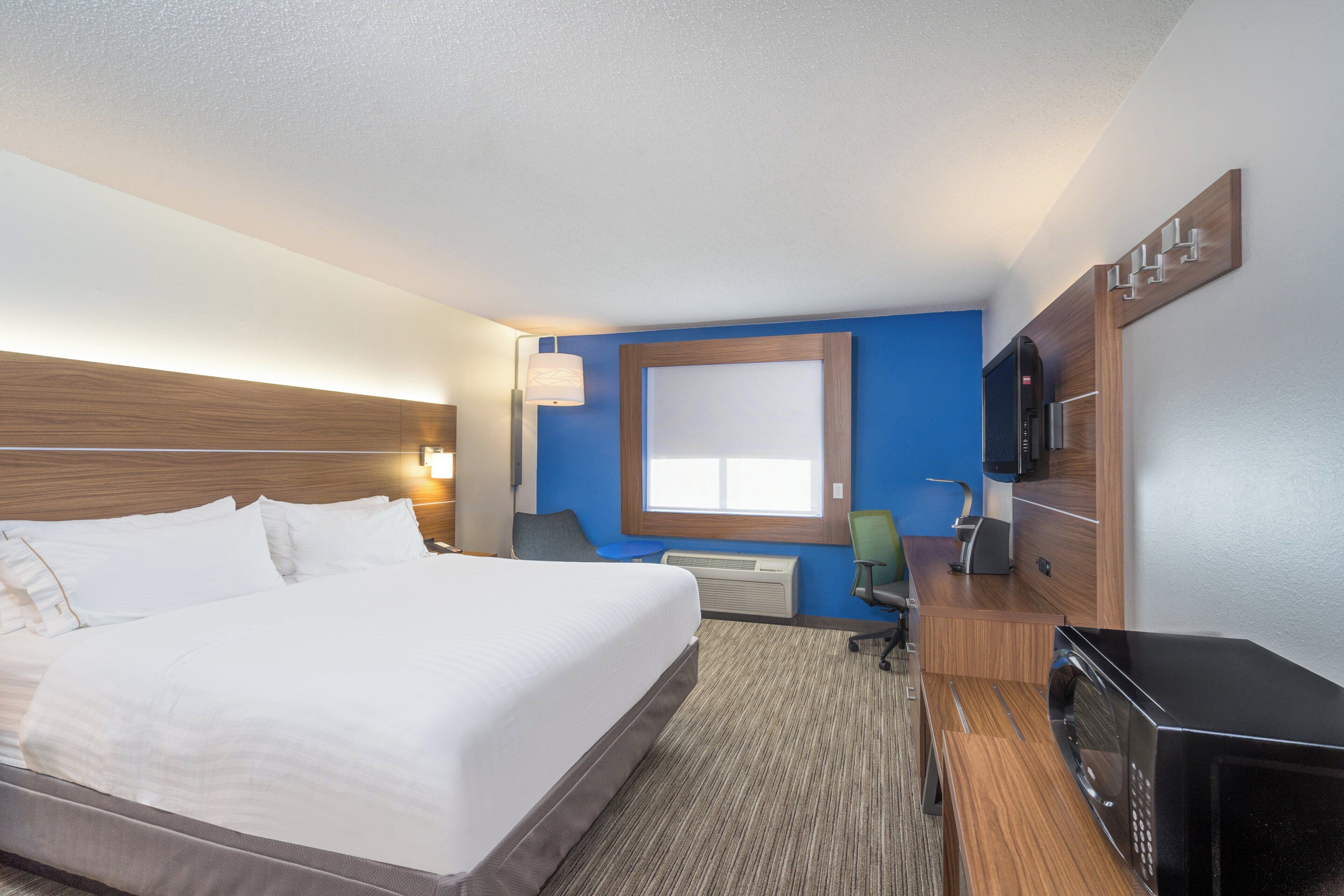 A hotel room with a bed, a desk, a chair, a television, and a window.