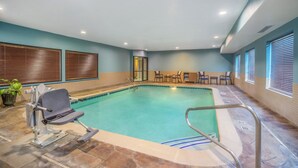 An indoor swimming pool with a lifeguard chair, a changing room, and a seating area with chairs and a table.