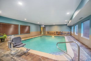 An indoor swimming pool with a lifeguard chair, a changing room, and a seating area with chairs and a table.