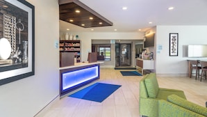 A reception area with a counter, a blue illuminated panel, a green sofa, and a television on a stand.