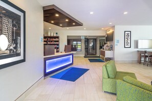 A reception area with a counter, a blue illuminated panel, a green sofa, and a television on a stand.