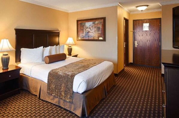A hotel room with a large bed, two bedside lamps, a wooden headboard, a patterned rug, and a framed picture on the wall. - Best Western Plus Southpark Inn & Suites (Tyler)