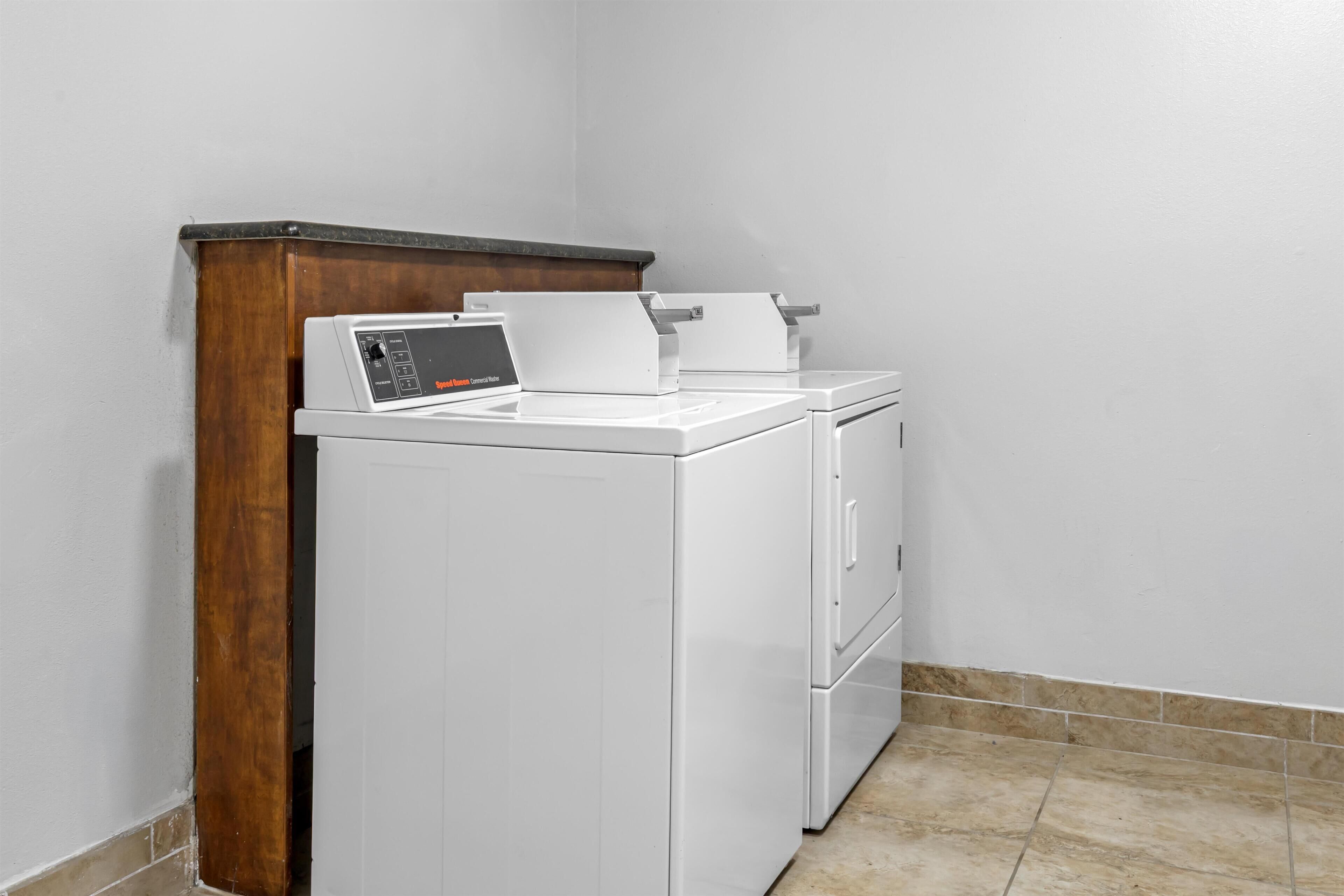 A laundry area with a washing machine and dryer, wooden cabinet, and tiled floor.