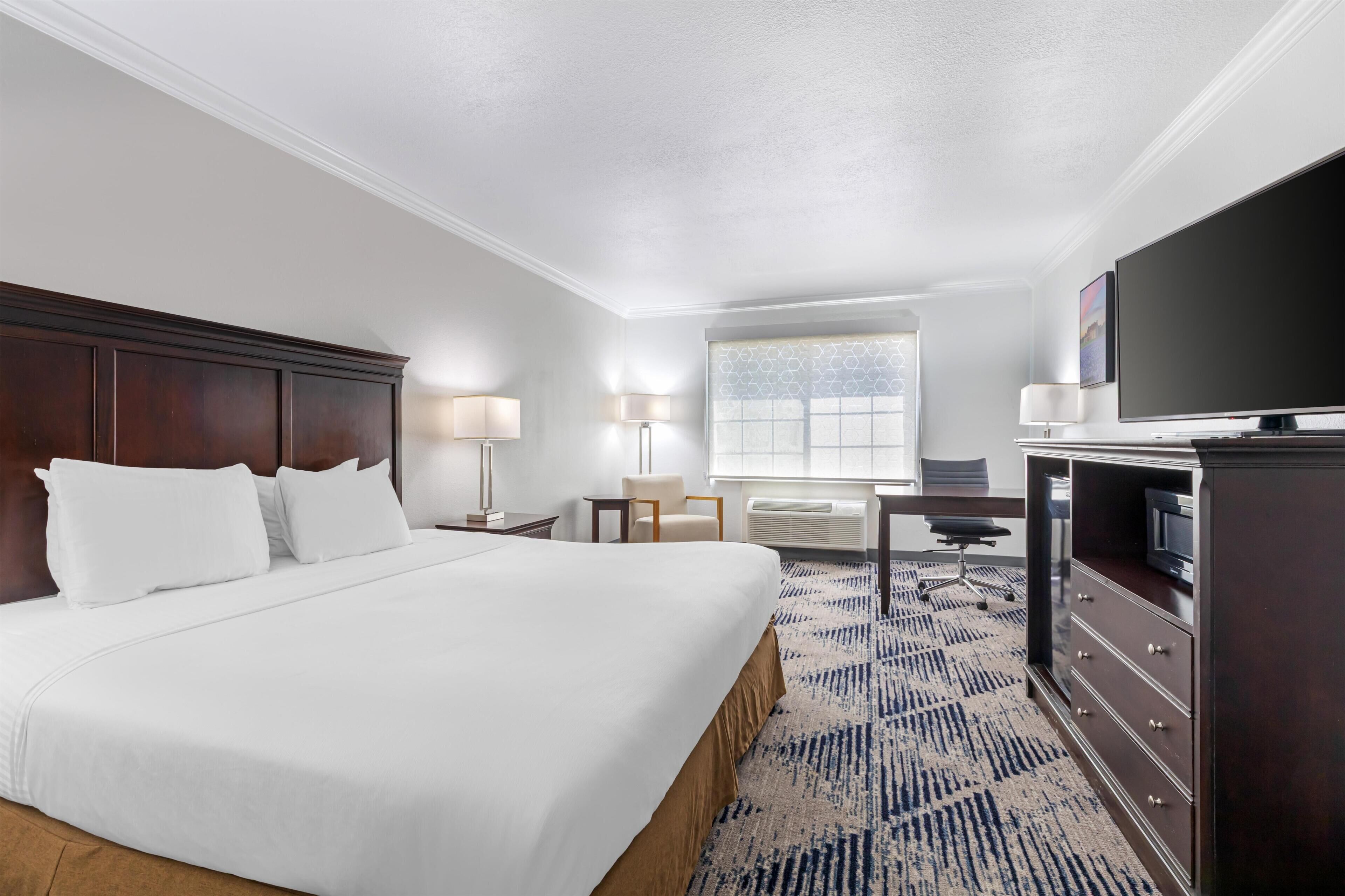 A hotel room with a large bed, a desk, a television, and a window.