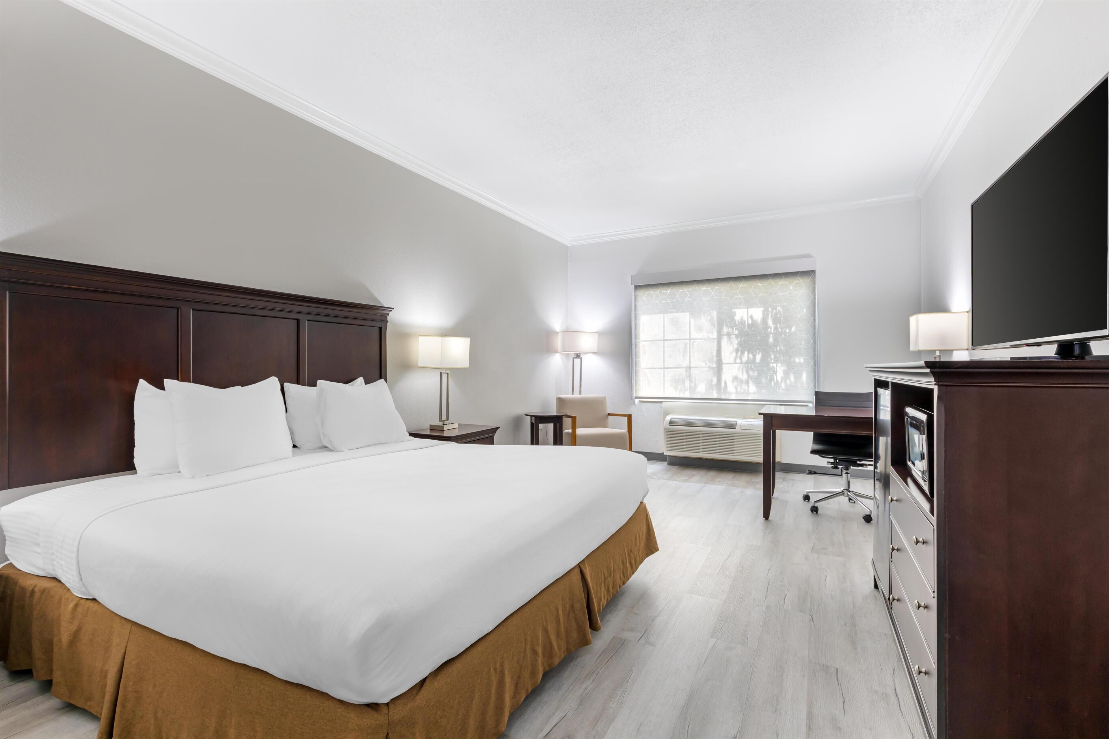 Habitación de hotel con una cama grande, un escritorio, una silla, un televisor y una ventana con cortinas.
