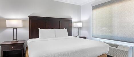 A hotel room with a large bed, two bedside tables, a window with a view, and an air conditioning unit.