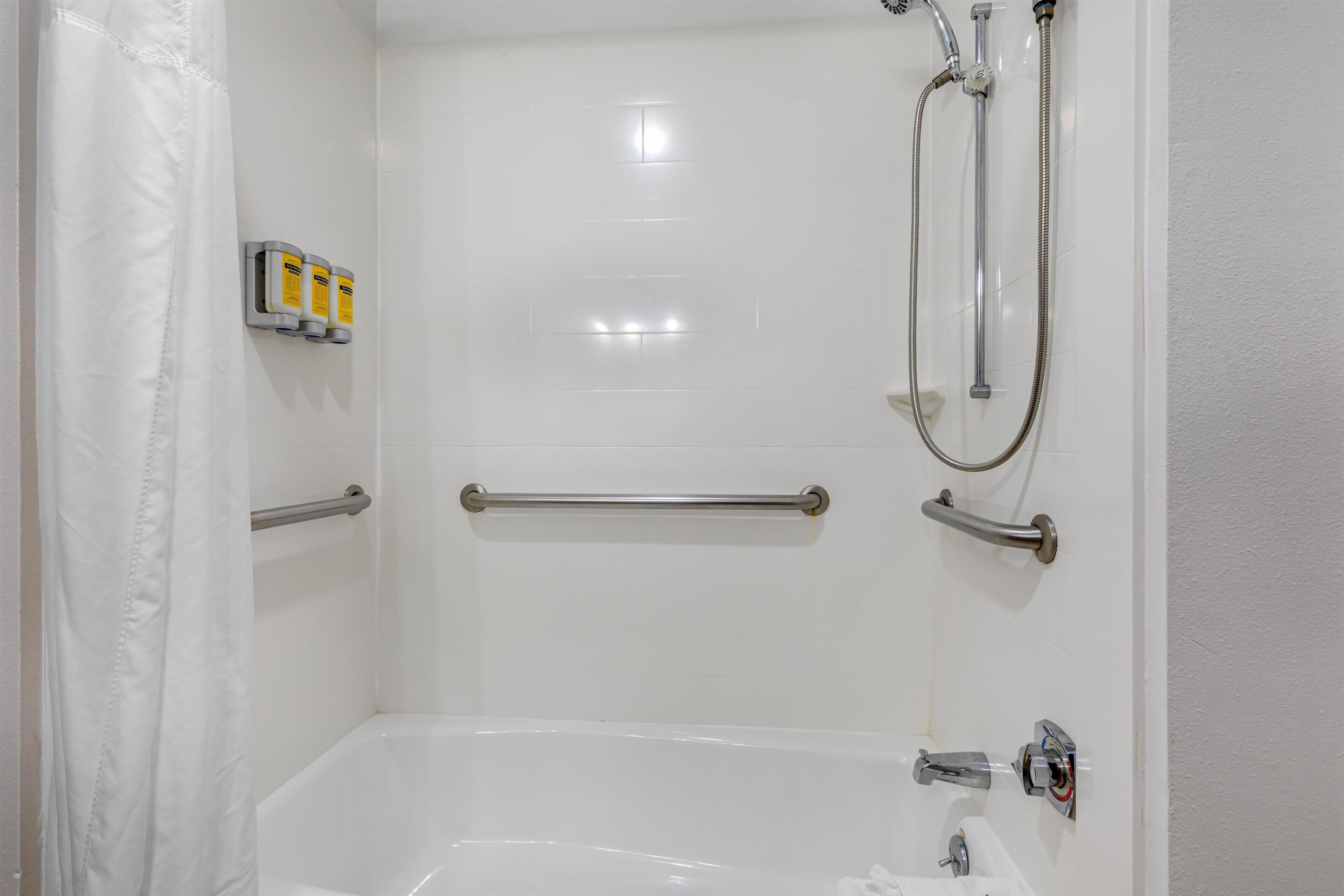 A white bathroom with a bathtub, a shower, and handrails.