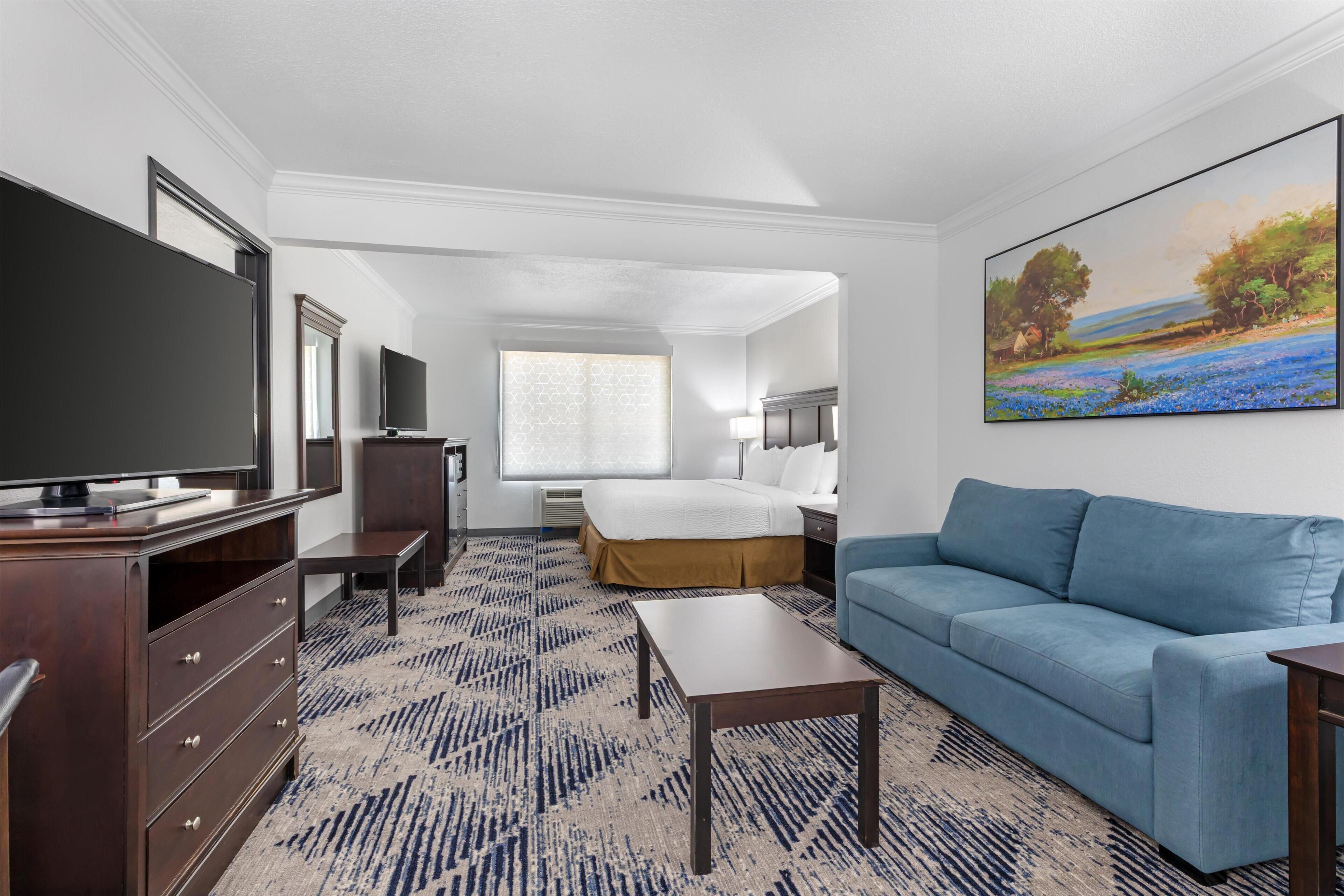 A hotel room with a bed, a blue sofa, a TV, a desk, and a painting on the wall.