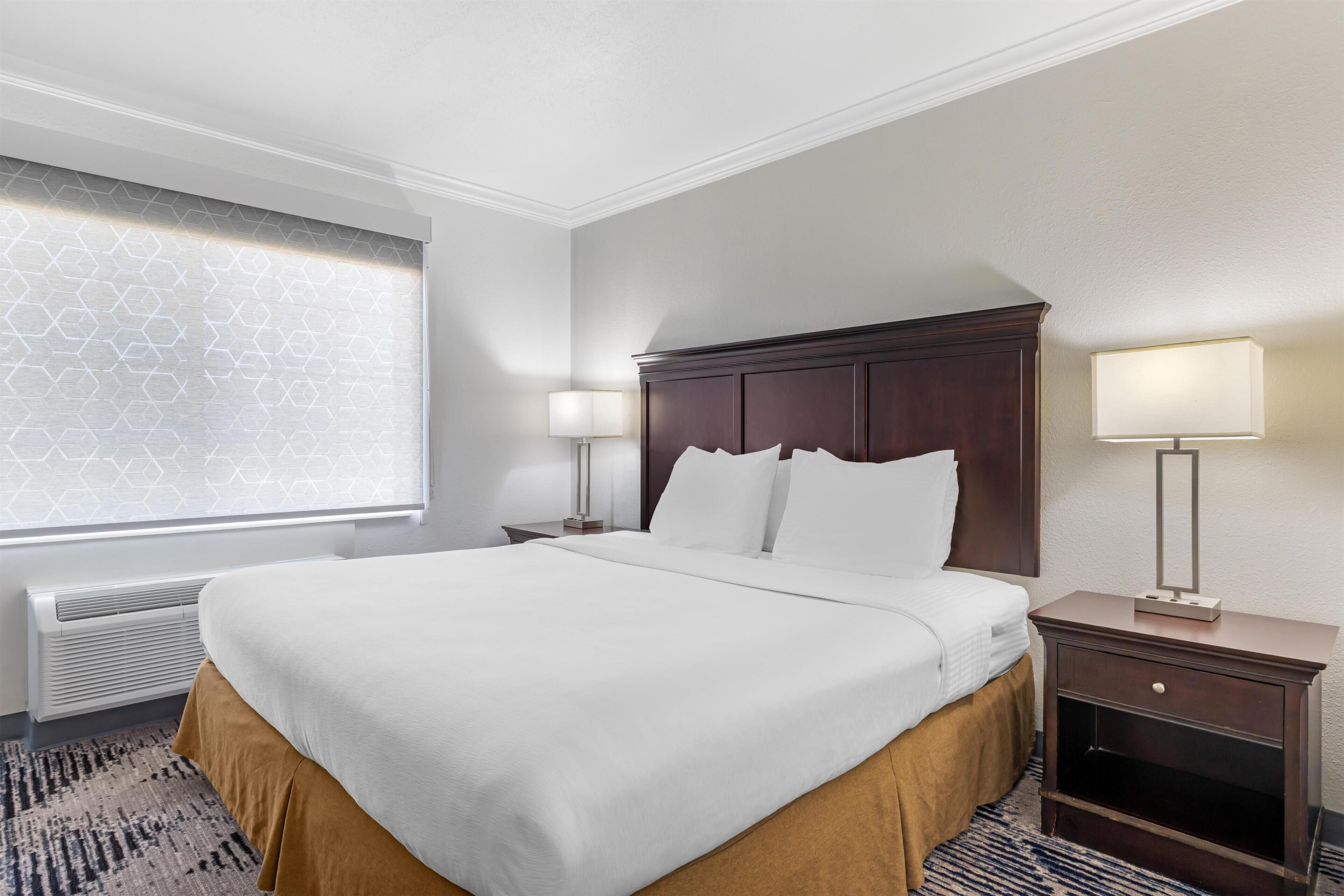 Une chambre d’hôtel avec un grand lit, deux tables de chevet, une fenêtre ornée d’un motif géométrique et un radiateur.