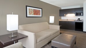 A hotel room with a sofa, a small table, a coffee machine, and a microwave in the kitchenette. - Holiday Inn Express Hotel & Suites Colby by IHG (Colby)