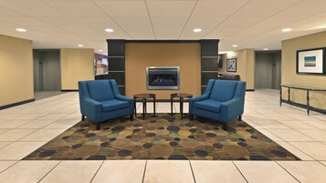 A lobby with two armchairs, a small table, a fireplace, and a patterned carpet.
