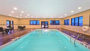A hotel swimming pool with a view of the city at dusk, a seating area with tables and chairs, and a lifeguard stand.