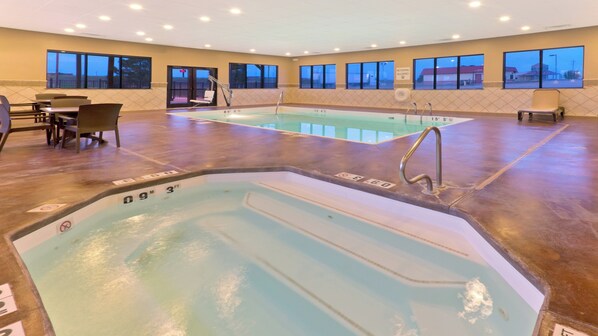 A hotel pool area with two pools, seating, and a view of the outside.
