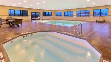 A hotel pool area with two pools, seating, and a view of the outside.