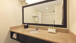 A bathroom with a sink, mirror, towel rack, and a shelf with toiletries. - Holiday Inn Express Hotel & Suites Colby by IHG (Colby)