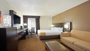 A hotel room with a bed, a desk, a television, a chair, a sofa, and a carpeted floor. - Holiday Inn Express Hotel & Suites Colby by IHG (Colby)