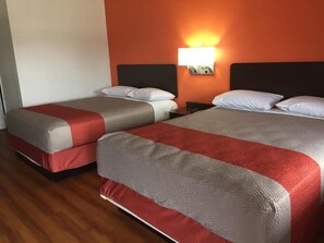 A hotel room with two beds, each with a red and grey bedspread, a nightstand, and a wall-mounted light. - Motel 6 Waco, TX (Waco)