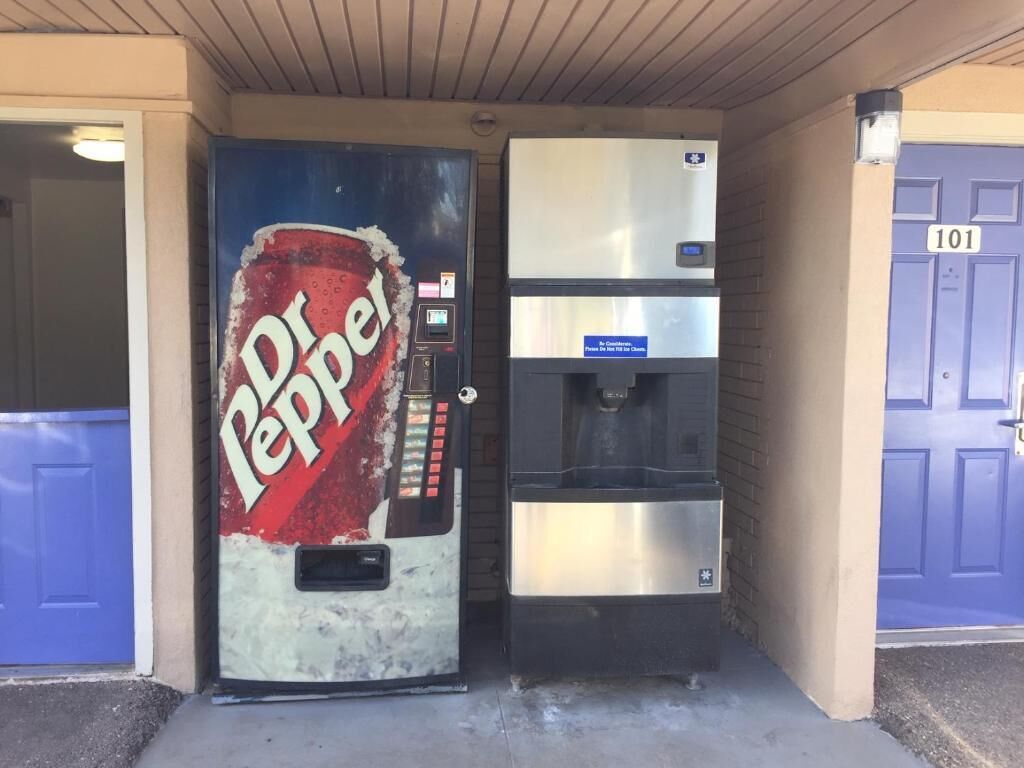 Una máquina expendedora de Dr Pepper y un dispensador de agua frente a un edificio con puerta azul.