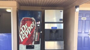 Ein Getränkeautomat mit Dr. Pepper und ein Wasserspender vor einem Gebäude mit einer blauen Tür.