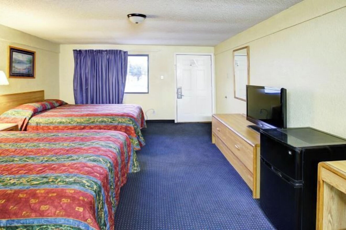 A hotel room with two beds, a television, a dresser, and a door.