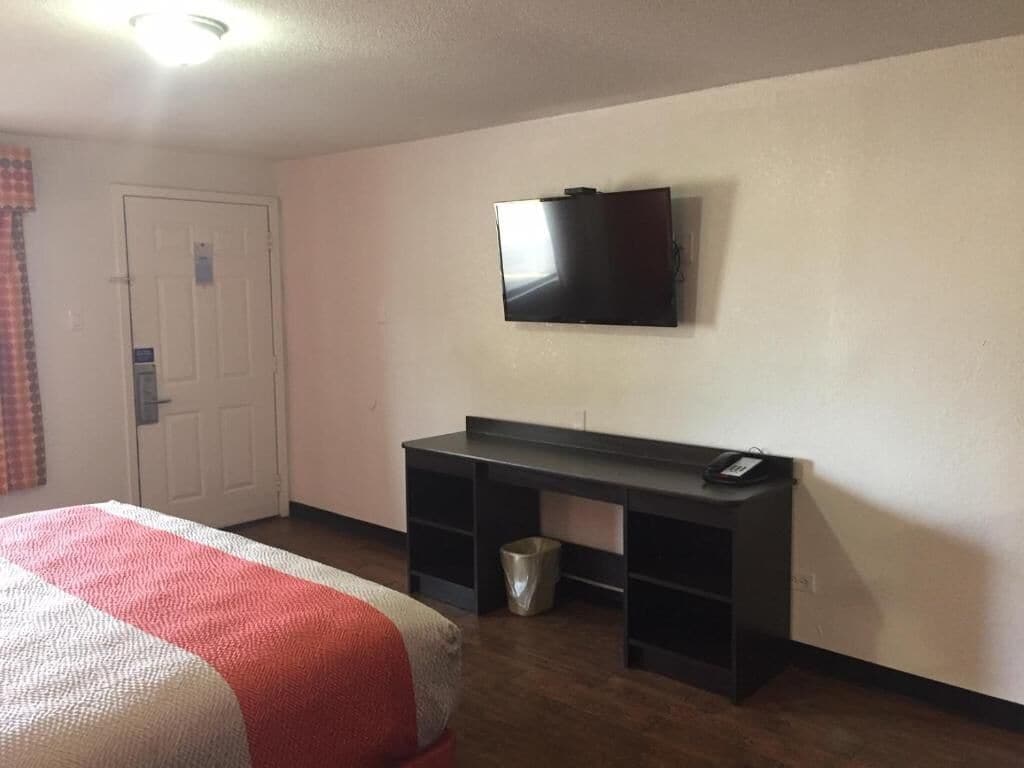 A room with a bed, a desk, a television, and a door.