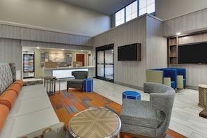 A hotel lobby with seating, a reception desk, a refrigerator, and a television. - Holiday Inn Express & Suites Atlanta N-Perimeter Mall Area by IHG (Atlanta)