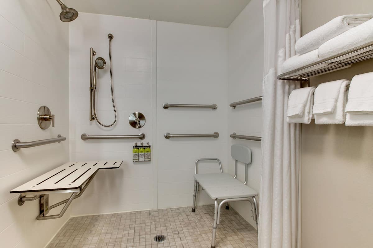 A modern bathroom with a shower, grab bars, a bench, and a towel rack.