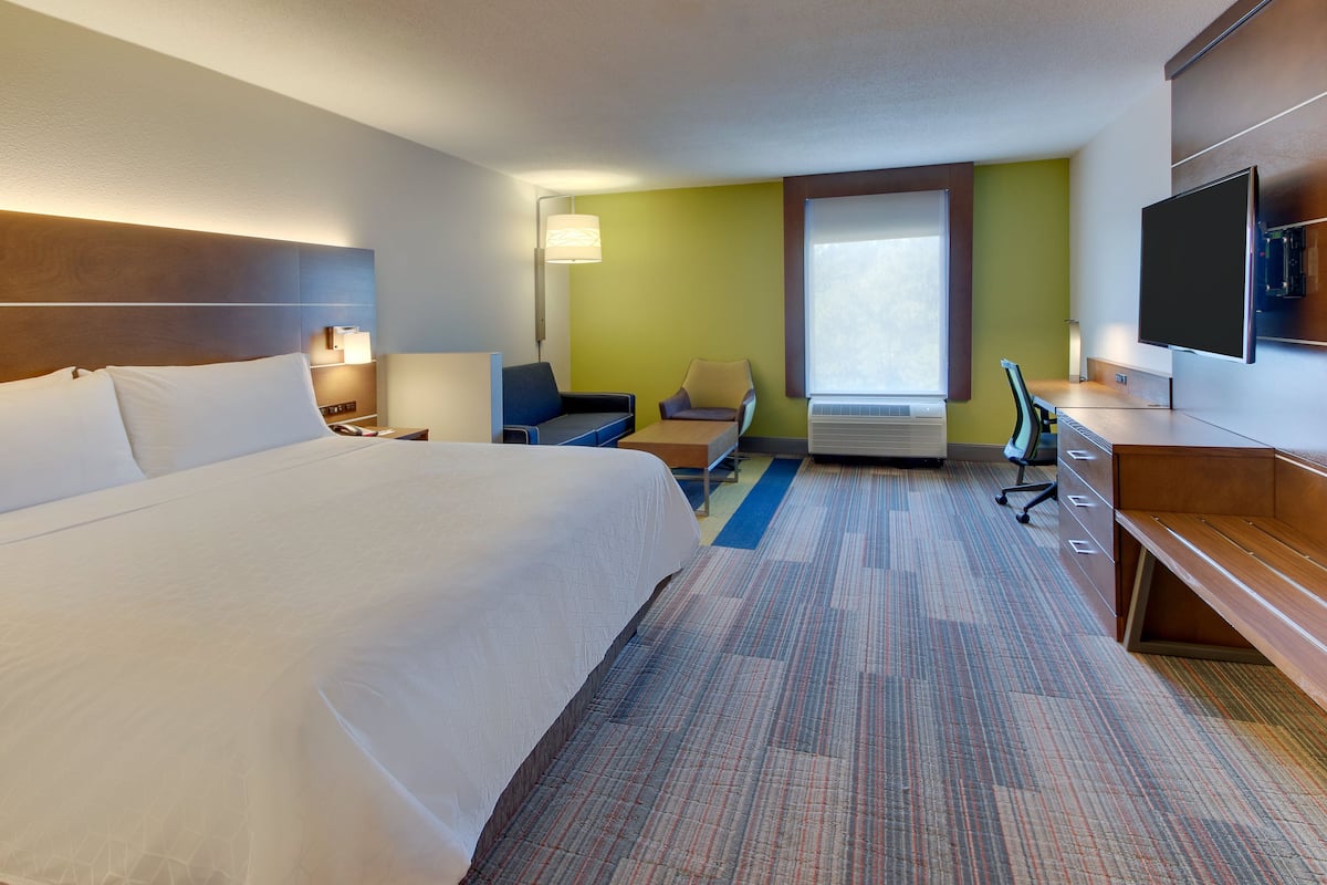 A hotel room with a large bed, a desk, a chair, a TV, and a window.