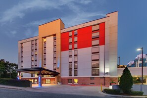 Un hôtel à plusieurs étages, doté d’une façade rouge imposante, d’une entrée couverte et d’un parterre aménagé devant l’entrée.