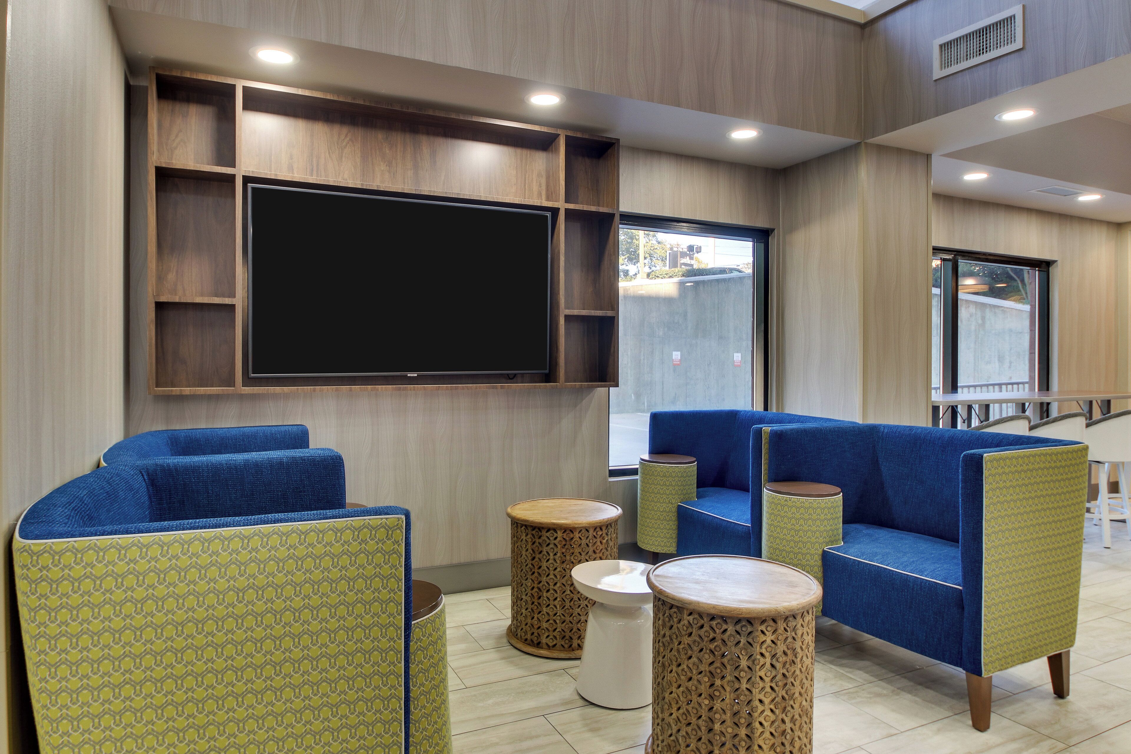 A modern lounge area with blue upholstered sofas, a large flat-screen TV, and decorative wooden accents.