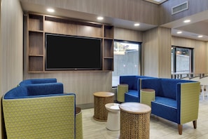 A modern lounge area with blue upholstered sofas, a large flat-screen TV, and decorative wooden accents. - Holiday Inn Express & Suites Atlanta N-Perimeter Mall Area by IHG (Atlanta)