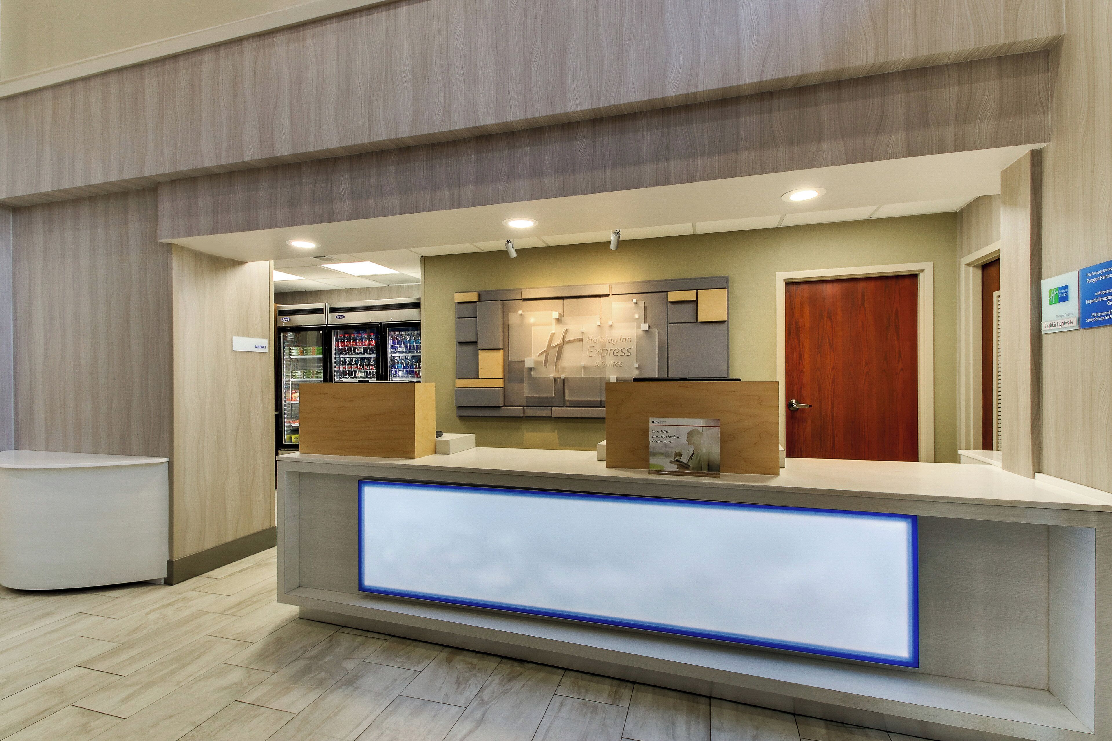 Un mostrador de recepción de hotel con una pantalla digital, un refrigerador y una puerta de madera.