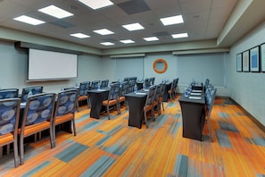 Une salle de conférence équipée de plusieurs tables et chaises, d’un écran de projection et d’un distributeur d’eau.
