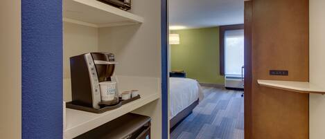A hotel room with a bed, a minibar, a coffee maker, and a view of the outside.