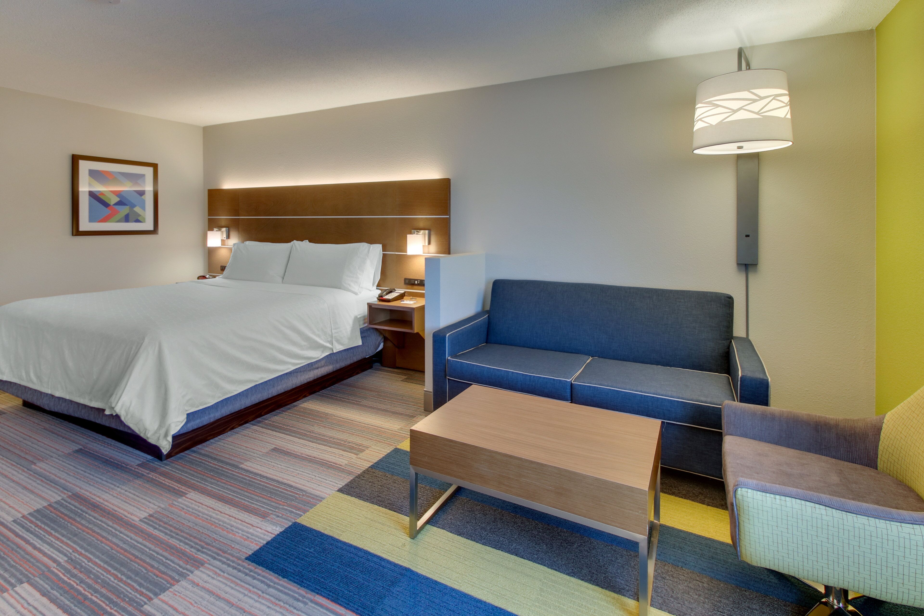 A hotel room with a bed, a sofa, a coffee table, and a lamp.