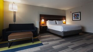 A hotel room with a bed, a sofa, a bench, a nightstand with a lamp, and a framed picture on the wall. - Holiday Inn Express & Suites Atlanta N-Perimeter Mall Area by IHG (Atlanta)