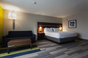 Ein Hotelzimmer mit Bett, Sofa, einer Bank, einem Nachttisch mit Lampe und einem gerahmten Bild an der Wand.