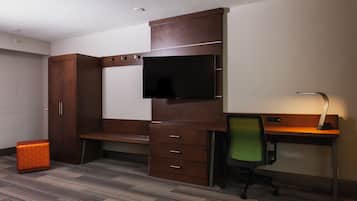 Una habitación de hotel con un escritorio de madera, una silla de oficina verde, un televisor en la pared y un armario.