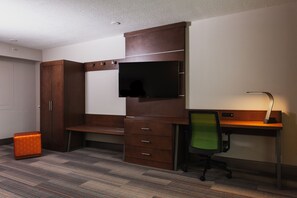 Ein Hotelzimmer mit einem Holztisch, einem grünen Bürostuhl, einem an der Wand befestigten Fernseher und einem Kleiderschrank.