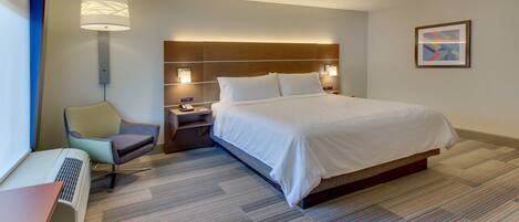 A hotel room with a large bed, a desk with a chair, a standing lamp, and a framed picture on the wall.
