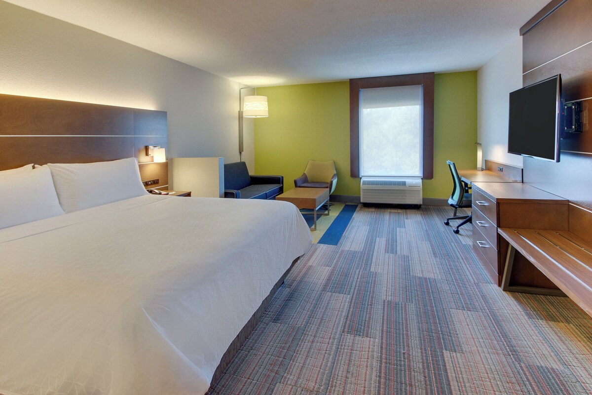Ein Hotelzimmer mit einem großen Bett, einem Schreibtisch, einem Sessel, einem Fernseher und einem Fenster.