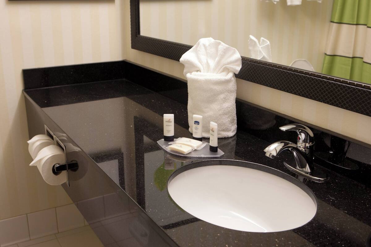 Une salle de bain avec un comptoir noir, un lavabo blanc, un miroir et des articles de toilette.