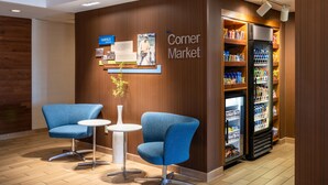 A corner market with two blue chairs, a small table, and a refrigerated display case. - Fairfield Inn and Suites by Marriott Denver Aurora/ Medical Center (Aurora)