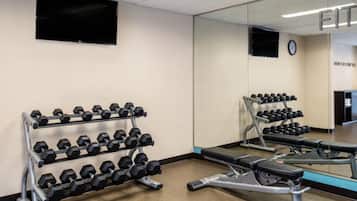 Un gimnasio con estantes para pesas, una prensa de banca y un muro con espejos.