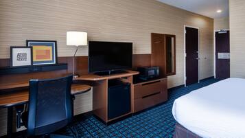 A hotel room with a bed, a desk with a TV, a microwave, a chair, and a wardrobe.